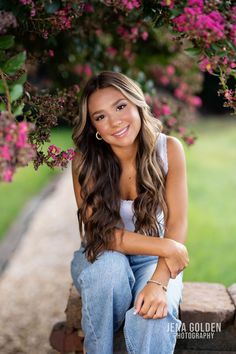 a beautiful young woman sitting on top of a wooden bench next to pink flowered trees