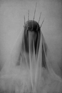 a black and white photo of a woman's head wearing a veil with spikes on it