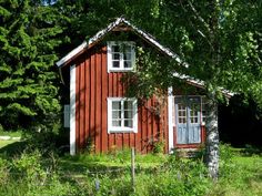 a small red house sitting in the middle of a lush green field next to trees