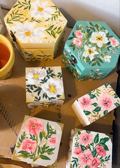 several boxes with flowers painted on them sitting next to a cup