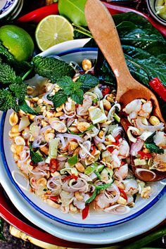 a white plate topped with salad next to limes and other foods on a table