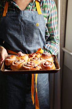 a person holding a tray with pastries on it in front of a window and wearing an apron