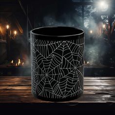 a black and white spider web trash can on a wooden table in front of a dark background