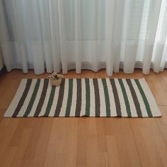 a striped rug on the floor in front of a window with white drapes and curtains