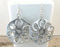 a pair of silver flower earrings sitting on top of a white display stand next to a wall