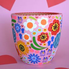 a colorful flower pot sitting on top of a pink surface with hearts in the background