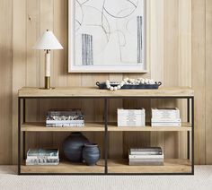 a book shelf with books and vases on it in front of a wall mounted painting