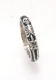 This is the middle width of my Memento Mori skeleton rings at 4mm wide. The Skeleton is flanked by crossed bones on one side and an hourglass on the other. Each ring in this collection is carved in wax by hand and cast using the ancient lost wax process. I then make a mold from which I can pull a wax copy of the original that can be resized to fit you and cast in silver or gold. These Skeleton rings are enameled with black glass in the recesses and polished to a high shine inside and brushed fin Skeleton Rings, Memento Mori Ring, Skeleton Jewelry, Dr Jewelry, Skeleton Ring, Wax Molds, Historical Jewellery, The Skeleton, Rings Rings