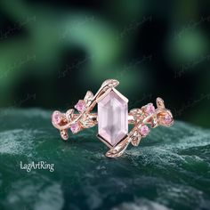 an image of a ring with pink stones on the front and side, sitting on top of a leafy green surface