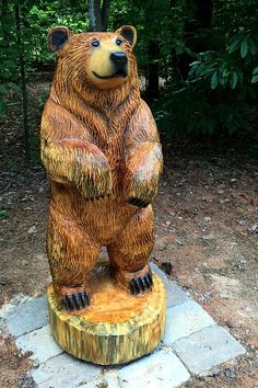 a statue of a bear sitting on top of a tree stump in front of some trees