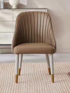 a beige chair sitting on top of a rug next to a white dresser and lamp