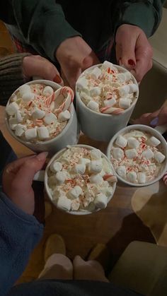 four people are holding cups with marshmallows and candy in them on a table