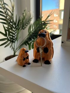 two small figurines sitting on top of a white table next to a window