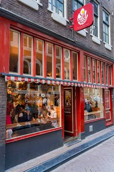 a red store front with people sitting in the window and on the sidewalk outside it