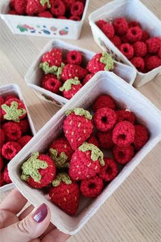 crocheted raspberries in small white containers on a table with one being held up to the camera