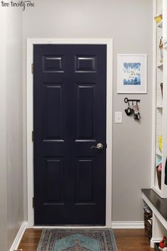 a blue door in a white room with pictures on the wall and a rug underneath it