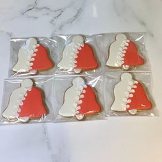 six decorated cookies in plastic wrappers on a marble counter top with white and red designs