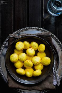 a bowl filled with yellow lemons on top of a table next to silverware