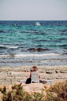 a little boy sitting on top of a beach next to the ocean with a boat in the distance