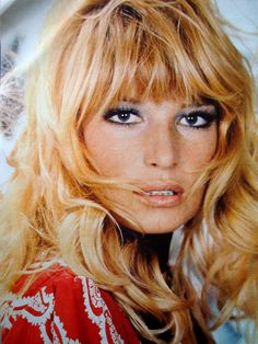 a woman with long blonde hair and blue eyes posing for a magazine cover photo in front of a red background