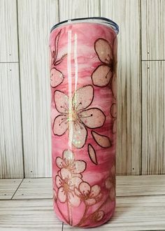 a pink tumbler with flowers painted on it sitting on a wooden table next to a wall