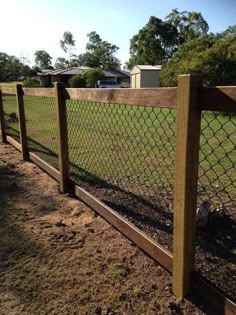 a fence that is in the dirt near some grass and trees with a house in the background