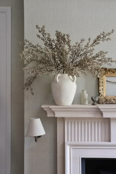 a white vase filled with flowers sitting on top of a mantel next to a mirror