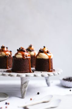 small chocolate cakes with caramel drizzle and whipped cream toppings on a white cake stand