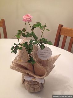 a pink rose in a burlap vase on top of a white tablecloth