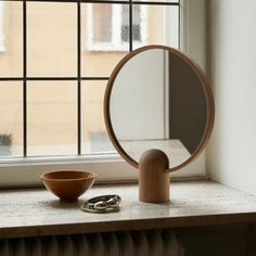 a round mirror sitting on top of a window sill next to a wooden bowl