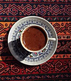 a cup of coffee sitting on top of a saucer next to a colorful rug