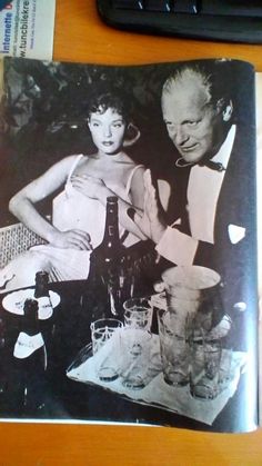 an old black and white photo of two people sitting at a table with wine glasses