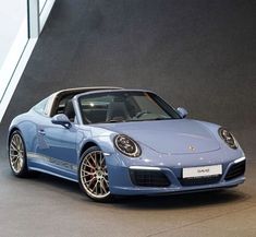 a blue porsche sports car parked in front of a building with windows on the side