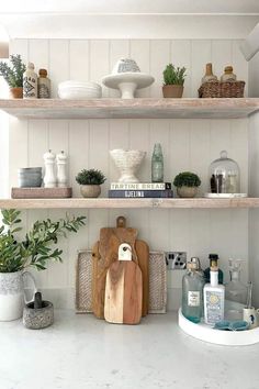 Immerse yourself in the aesthetic appeal of reclaimed oak shelves seamlessly integrated into a tongue and groove-paneled wall. Artfully adorned with vintage pieces, verdant plants, and carefully arranged books, these shelves embody the essence of modern farmhouse flair. A round white tray, layered cutting boards, and a pitcher housing olive tree branches contribute to the display’s sophistication. Kitchen Shelving Ideas, Kitchen Shelving, White Tray, Shelving Ideas, Oak Shelves, Reclaimed Oak, Olive Tree, Farmhouse Kitchen, Tree Branches