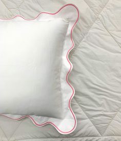 a white pillow with pink scalloped edges on a bed