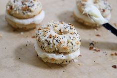 three donuts with white frosting and sprinkles are on a piece of parchment paper