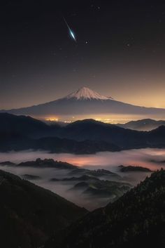 the night sky is filled with clouds, mountains and a distant object in the distance