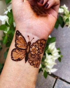 a woman's wrist with a butterfly tattoo on the wrist and flowers in the background