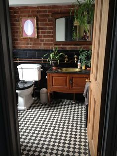 a bathroom with black and white checkered flooring next to a brick wall in the corner