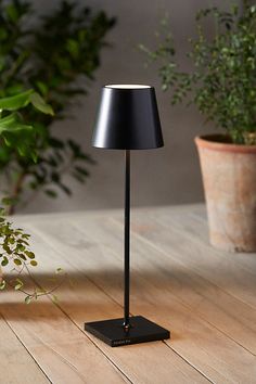 a black lamp sitting on top of a wooden floor next to a potted plant