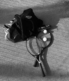 black and white photograph of tennis rackets on the ground next to a duffel bag