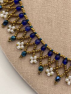 a blue and white beaded necklace on a beige cloth with gold chains, beads and pearls