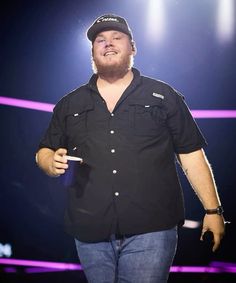 a man in black shirt and hat standing on stage holding a microphone with one hand