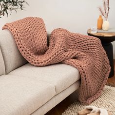 a couch with a blanket on top of it next to a table and potted plant