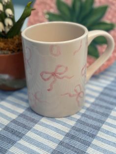 a coffee cup sitting on top of a blue and white table cloth next to a potted plant