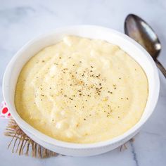 a white bowl filled with soup next to a spoon on top of a marble counter