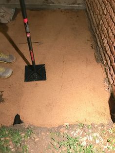 a person using a shovel to clean the floor in front of a brick wall with grass and dirt around it