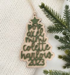 a wooden ornament hanging from a christmas tree on a white blanket next to a pine branch