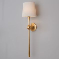 a gold wall light with a white shade on the side and a gray wall behind it