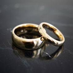 two gold wedding rings sitting on top of a black table next to eachother